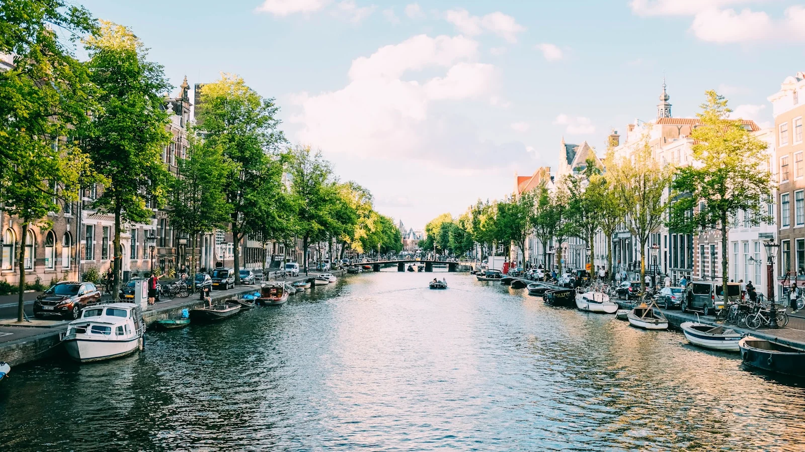 A row of 17th-century gabled merchant houses lining one of Amsterdam's central canals, with bicycles parked along the railings and a houseboat moored on the water.