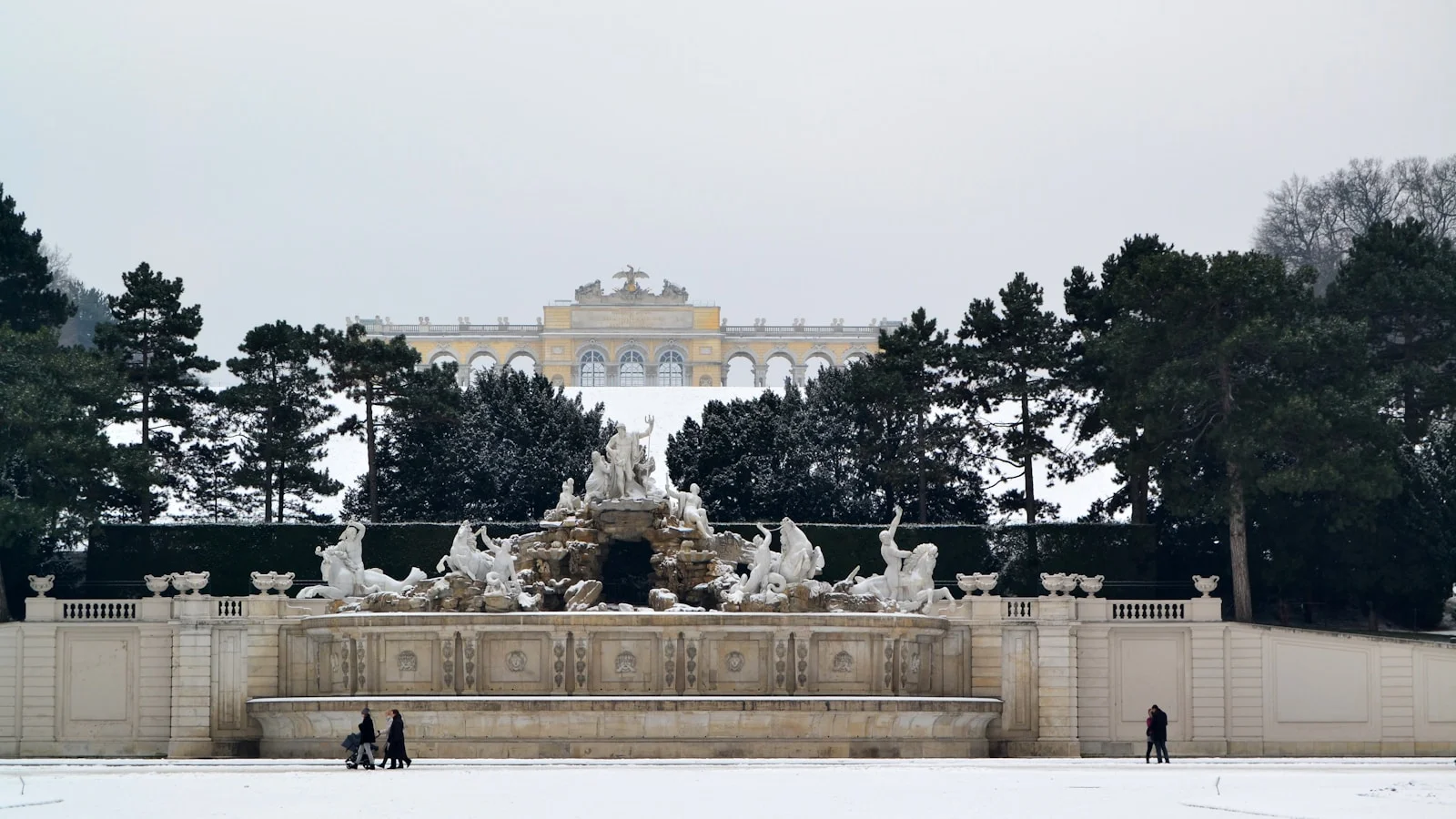 Schönbrunn Palace in Vienna seen from the Gloriette hilltop, with the yellow Baroque facade fronting formal hedge gardens and the city stretched out behind.